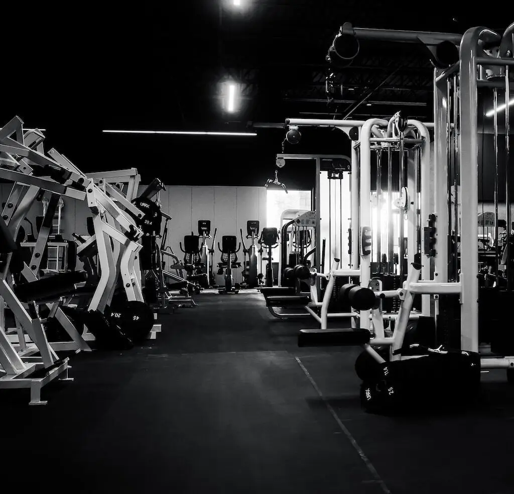 An empty training floor at Rhein Athletic Club, rows of weight machines under dramatic overhead lighting against a dark ceiling.